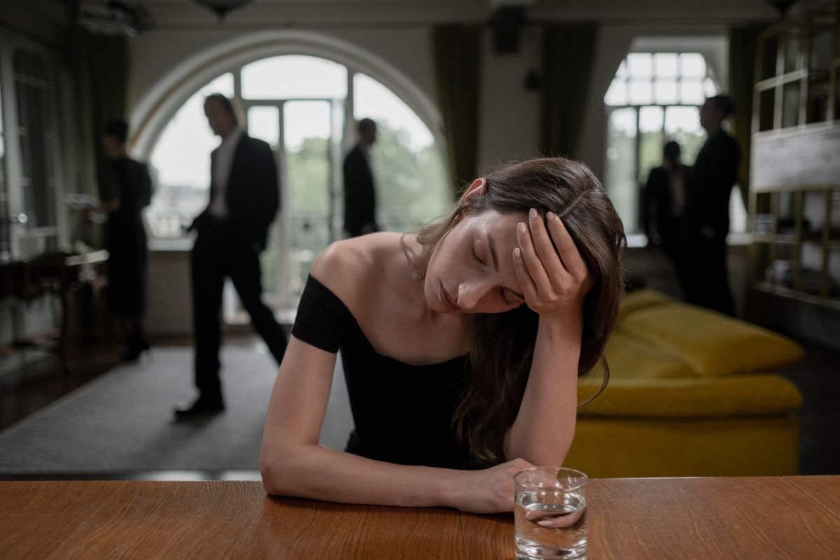 depressed woman sitting at a table while life carries on behind her