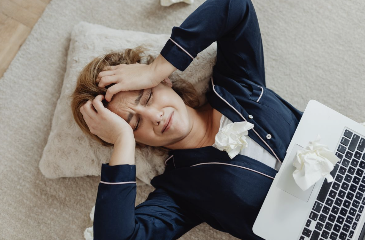 stressed woman lying on her back while an open laptop sits on her stomach