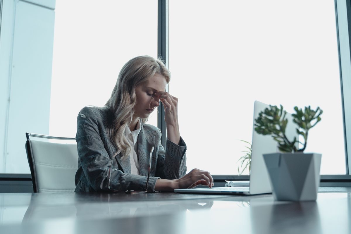 woman pinching the bridge of her nose as she works on a laptop