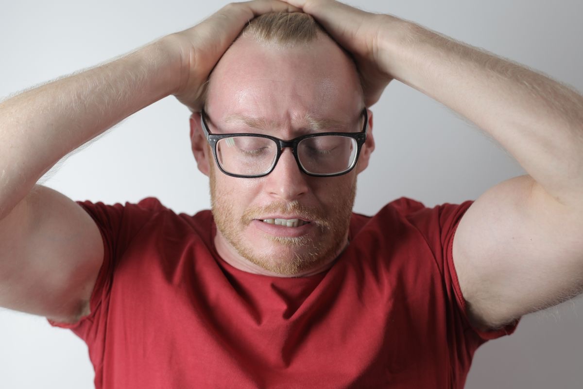 man holding his head, looking at his laptop with an anxious expression