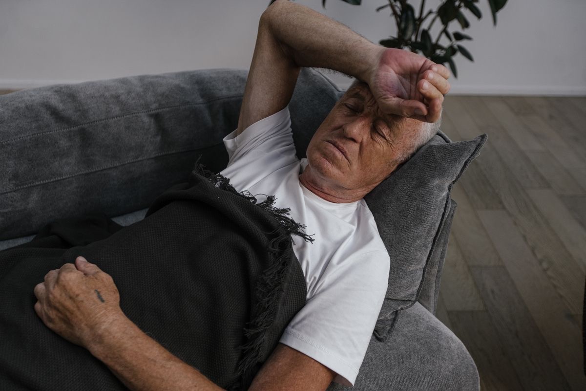 man lying on a couch with one arm over his forehead in a gesture of exhaustion