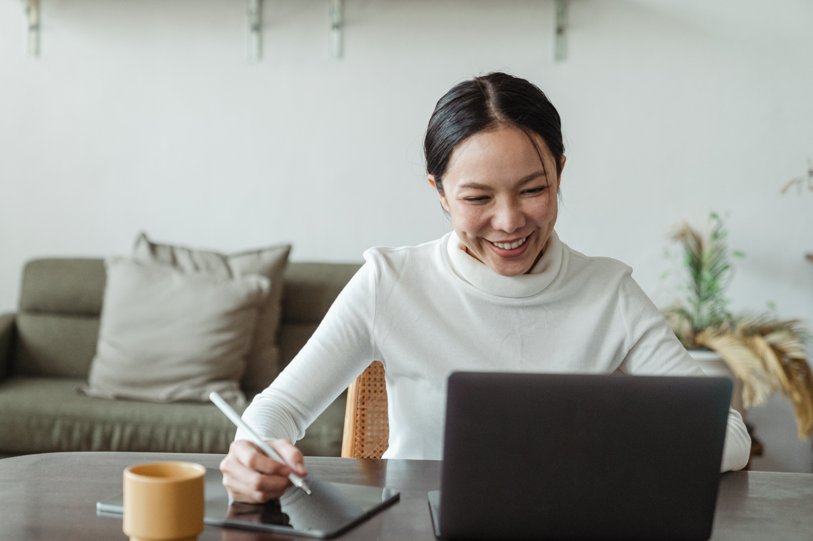 Person smiling while working on a laptop at a desk with a notebook and coffee mug, symbolizing strategic business planning