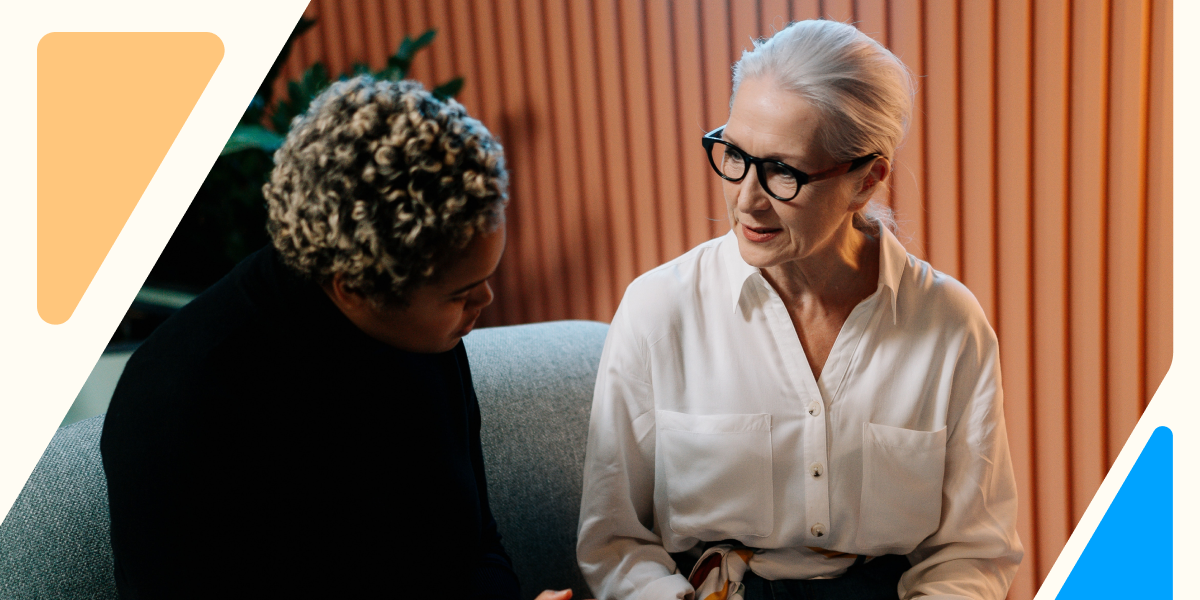 Two colleagues sitting together and having a thoughtful conversation, symbolizing workplace support and empathy for employees managing cancer and its impact on mental health.