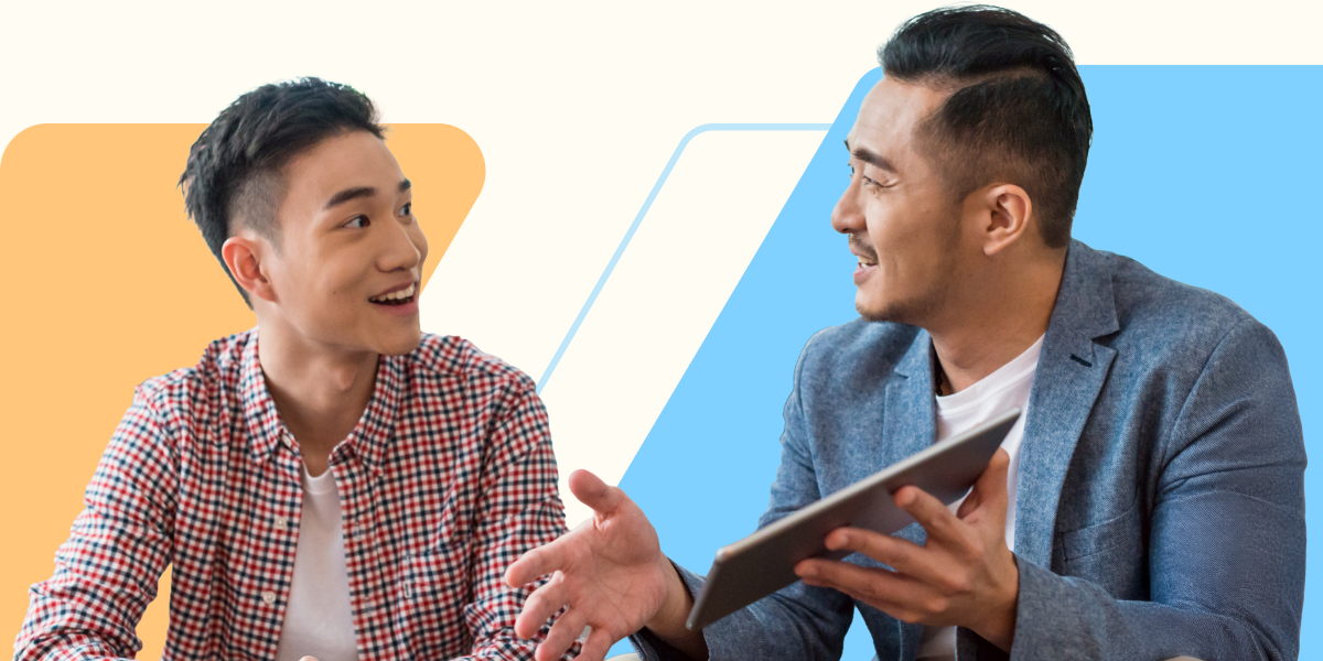 Two colleagues sit and talk in a friendly, engaged conversation. One person holds a tablet while the other smiles and listens. The background features abstract geometric shapes in orange and blue.