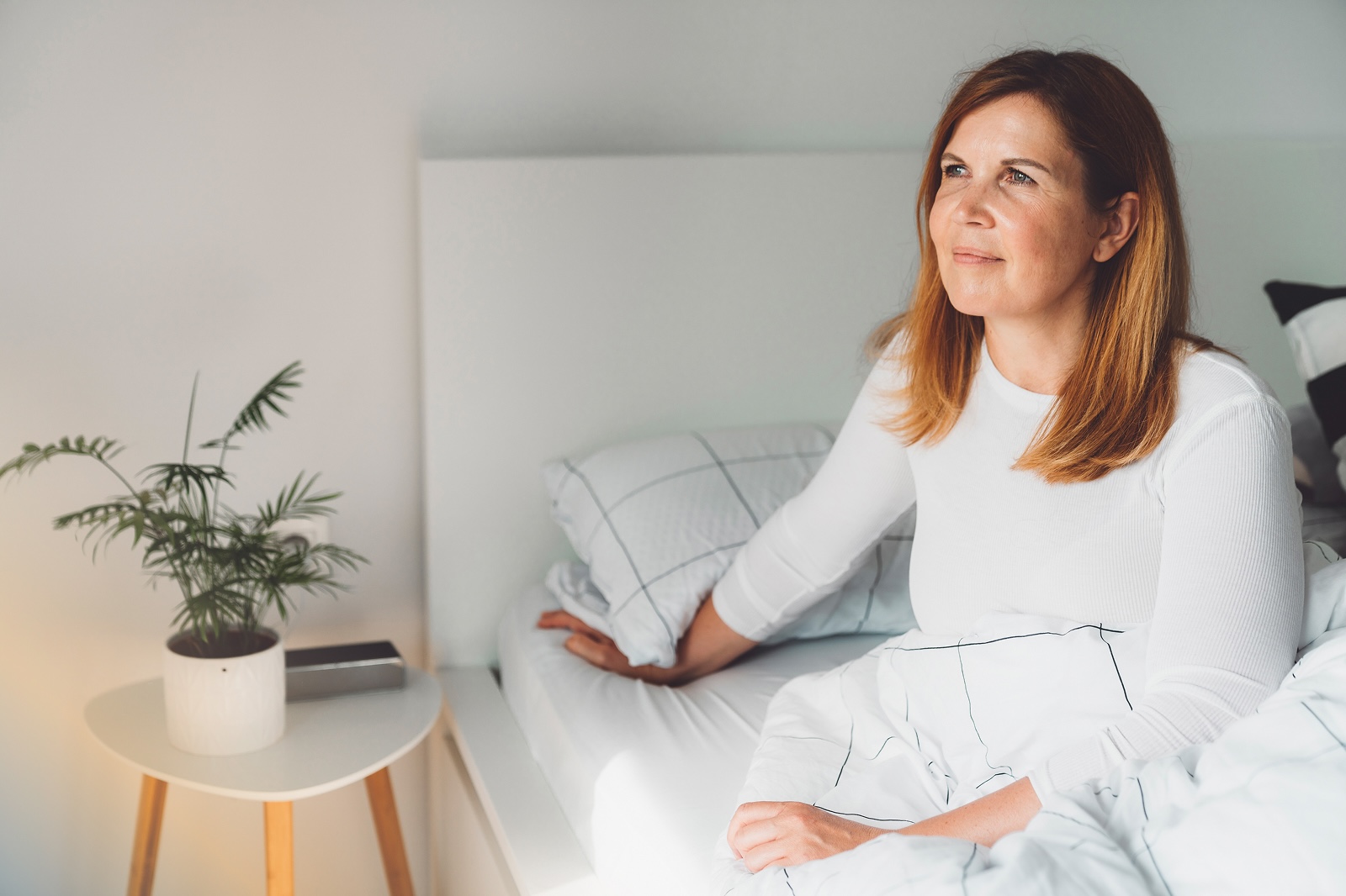 Woman sitting up in bed in a calm bedroom, appearing rested and reflective