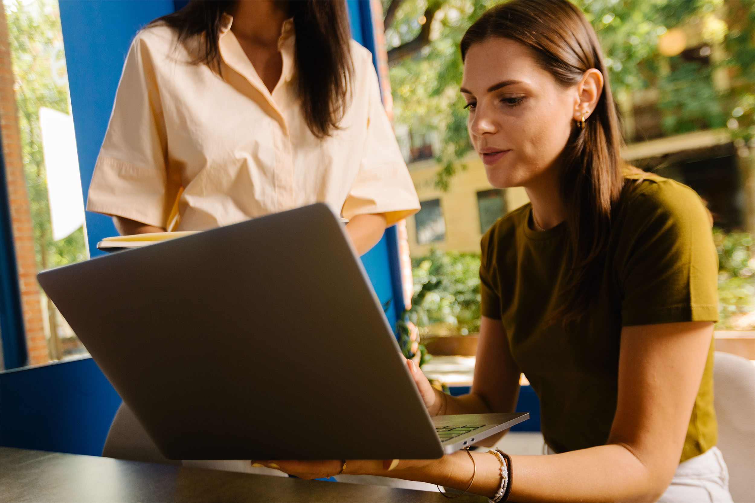 A woman gathering information on her laptop with a colleague in the background