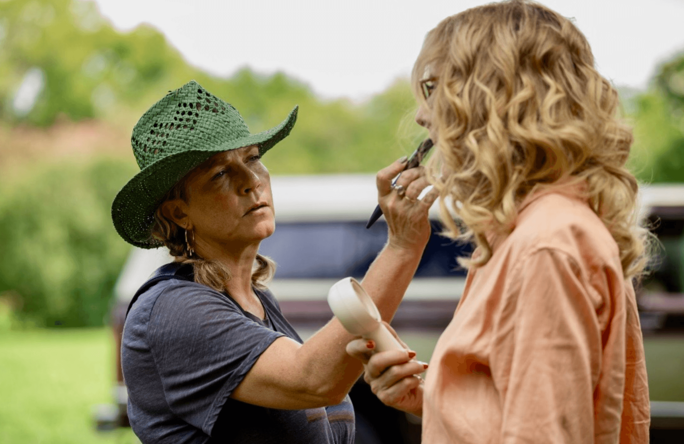 Shelley Illmensee on set wearing a green cowboy hat focused on touching up an actor between takes.