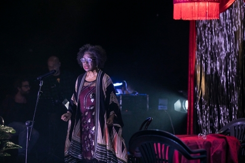 Valois Mickens (Esme), a Black woman, is on stage with a microphone