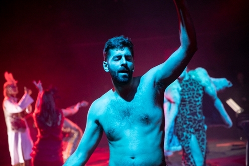 Ivan Mihailović (Solider), a white man, is shirtless and in foreground in blue light, other performers in background