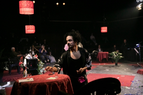 John Maria Gutierrez (Pylade), a young Dominican man, on stage, seated at a red table