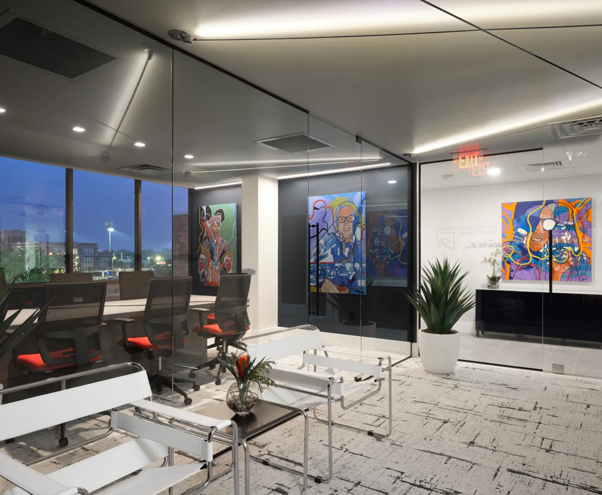 Commercial Architecture photo of Suarez Architecture office. Modern office conference room with glass walls, white chairs, colorful artwork, and city view at dusk.