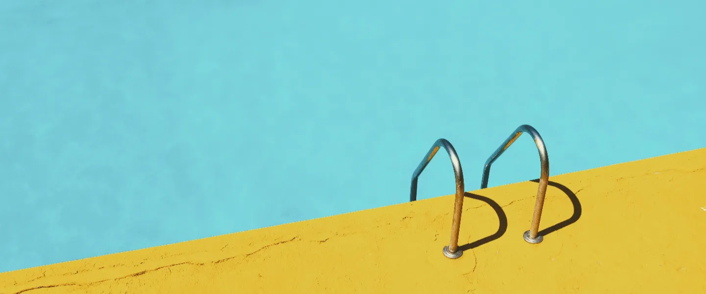 Imagen cenital de una piscina con el agua calma donde se ve la escalera y el borde amarillo