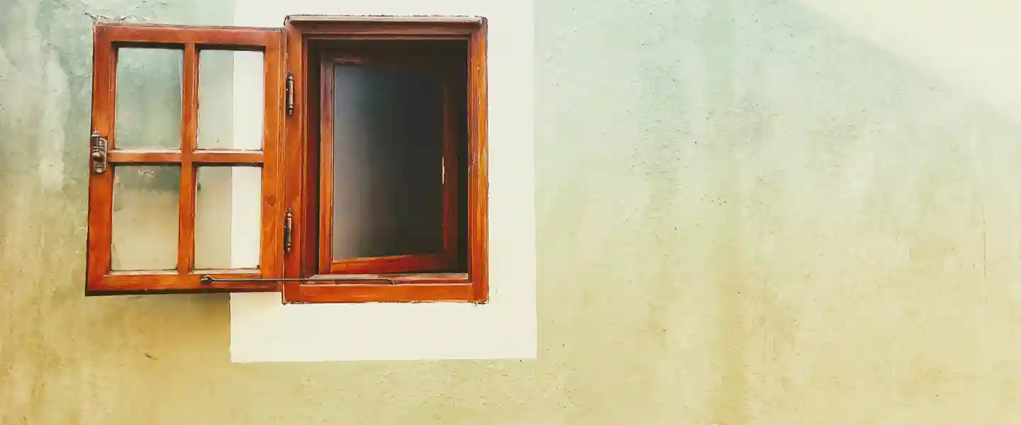 Pared exterior de una casa en la que se ve una pequeña ventana de madera abierta