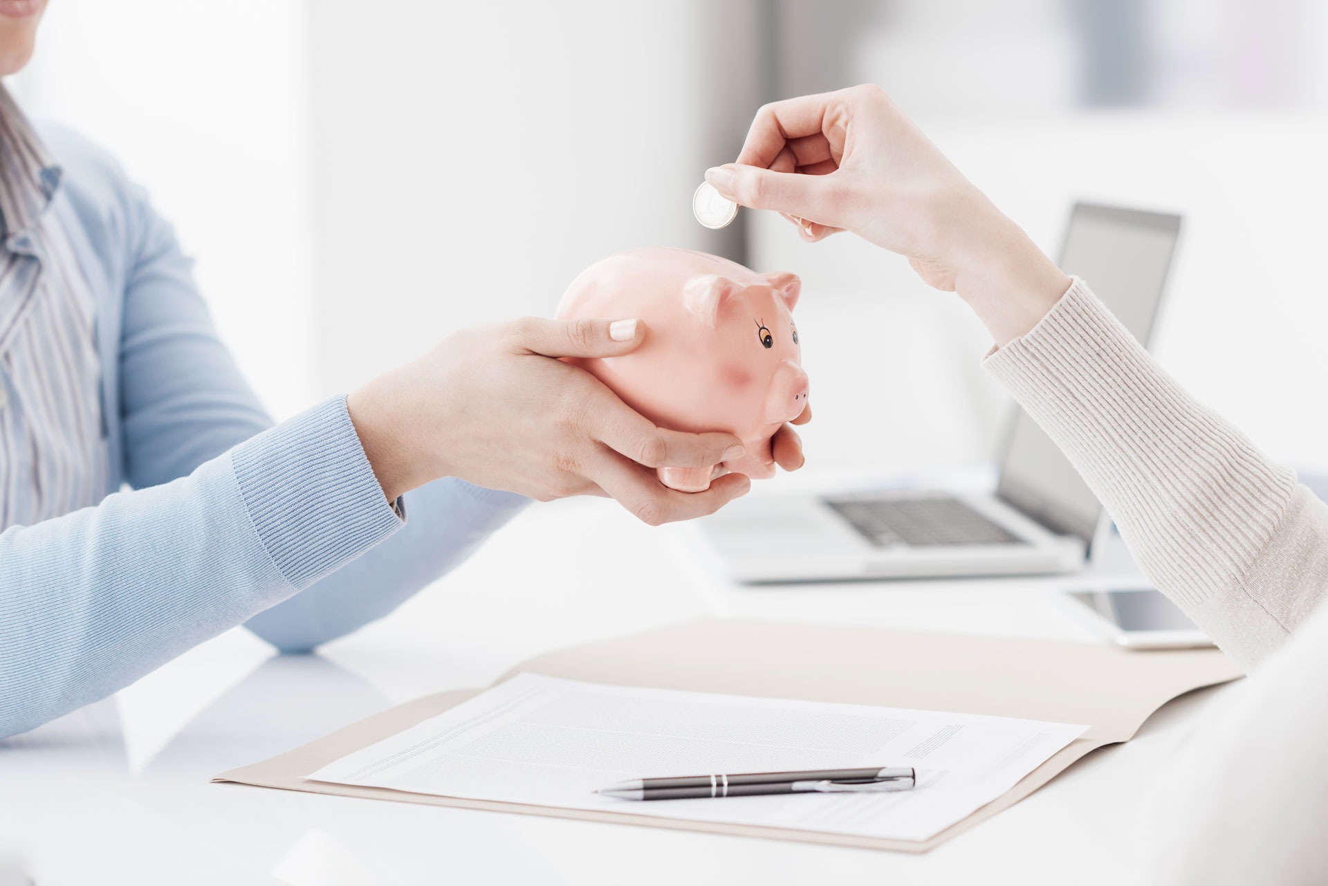 Financial advisor holding a piggy bank and customer inserting a coin: deposit, savings plan and retirement fund concept