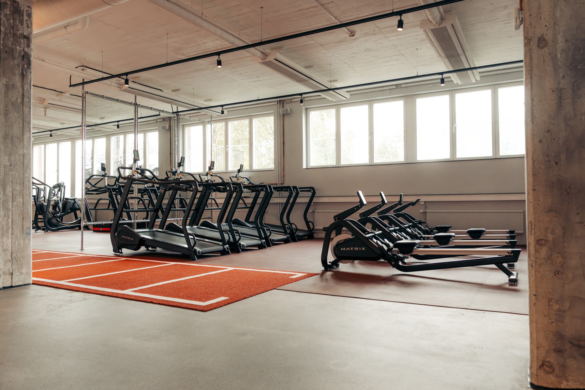 Cardio equipment beside broad windows and a marked red exercise area.