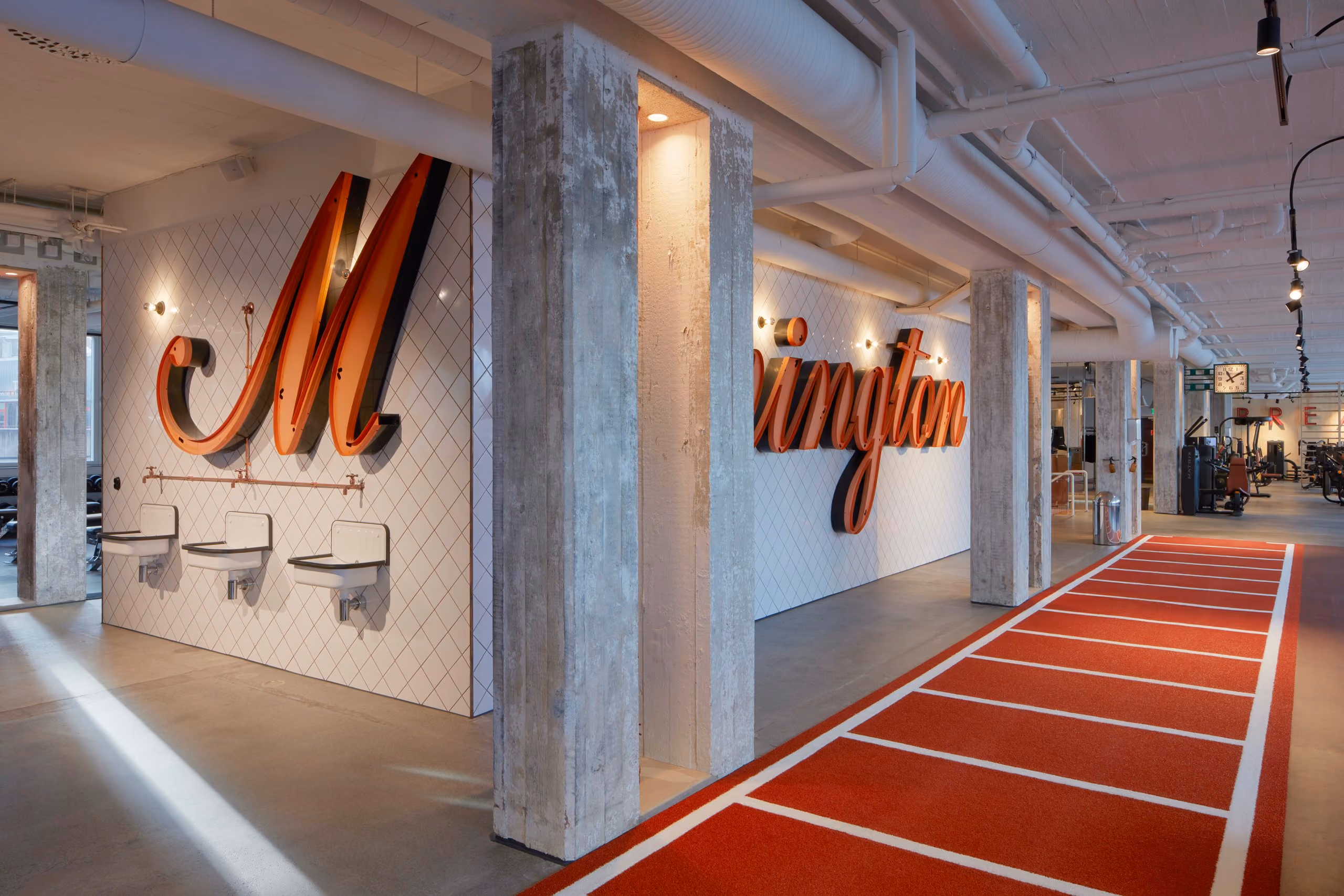 Mornington Health Club Bromma training floor with a red running lane, concrete columns and large illuminated Mornington lettering.