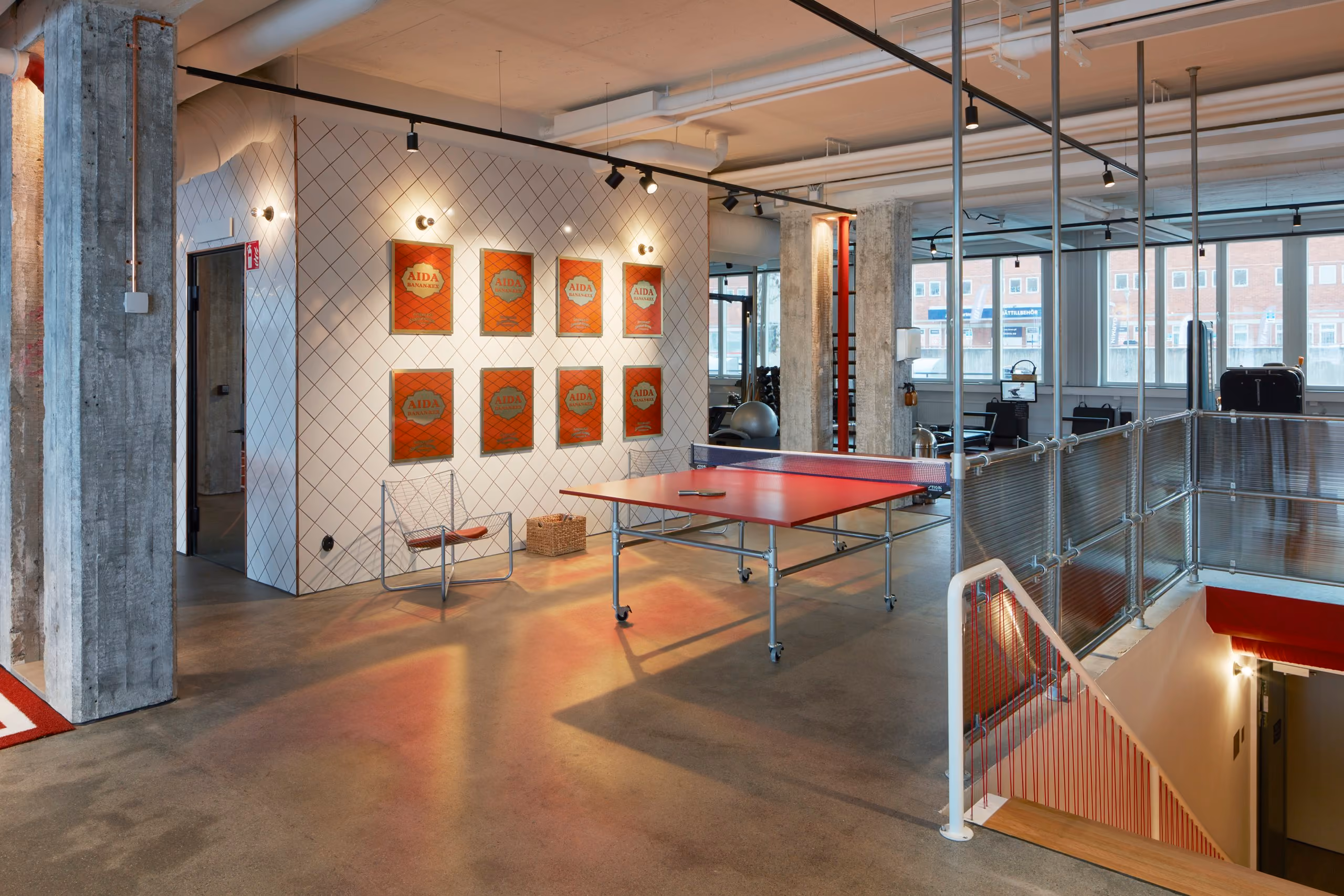 Table tennis and open circulation around the central stair, framed by concrete columns and red graphic details.