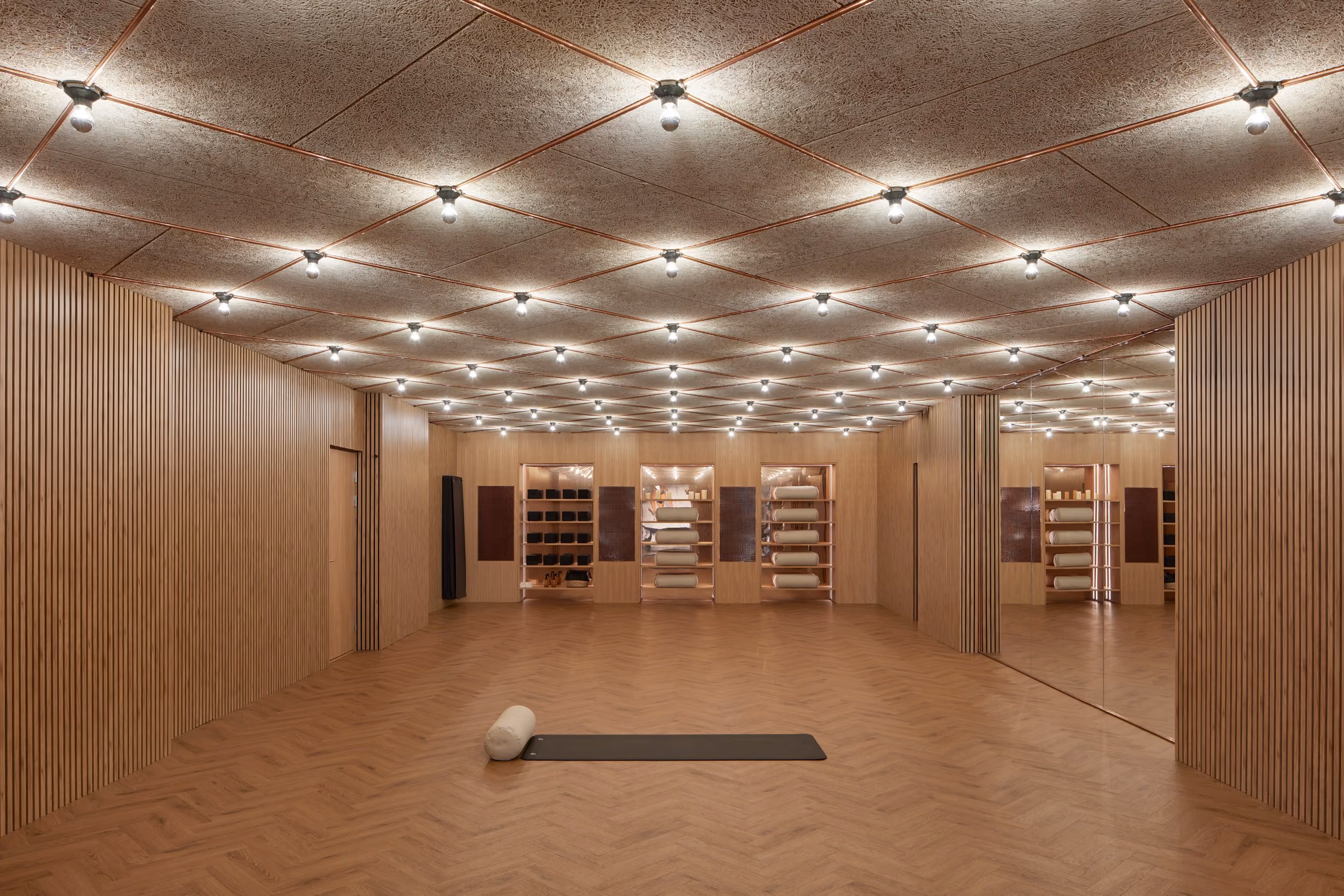 Empty timber-lined studio with herringbone flooring, mirrors and a geometric pattern of warm ceiling lights.