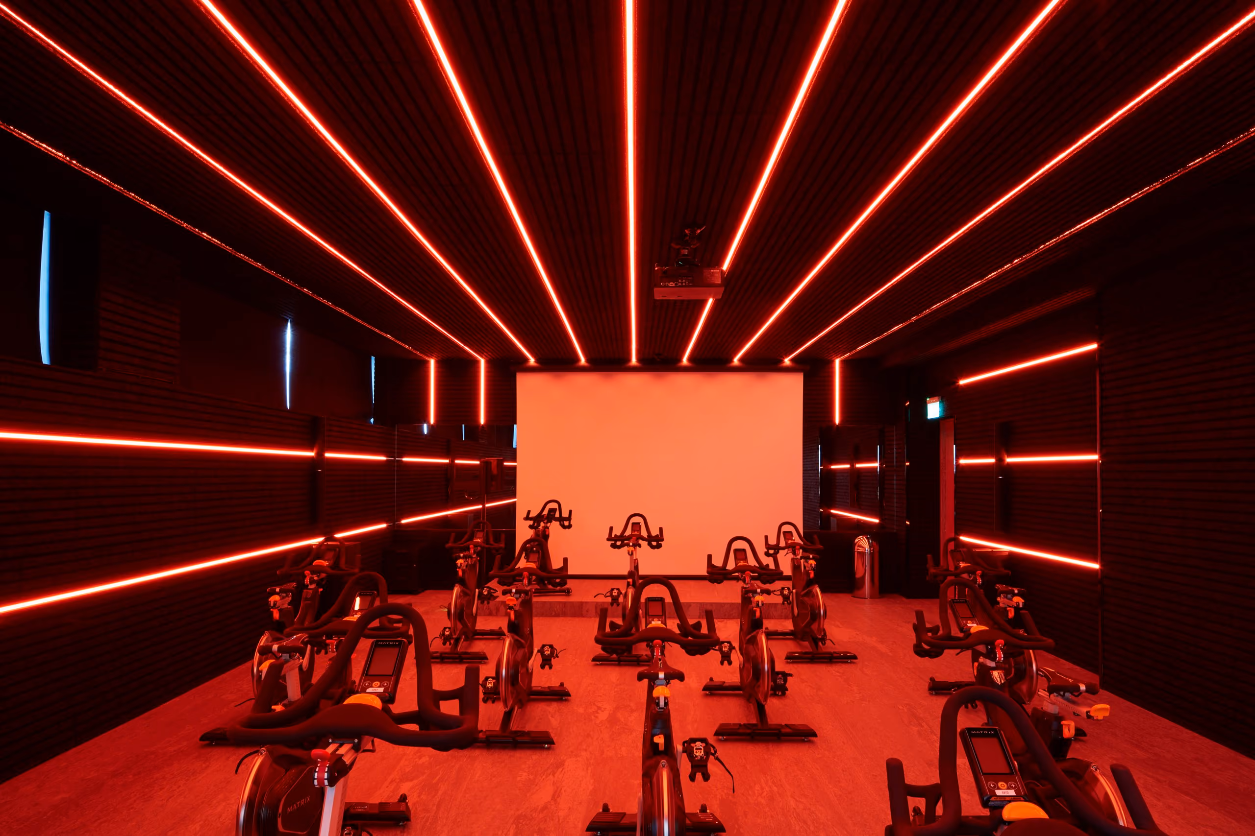 Rows of stationary bikes framed by vivid red linear lighting in the cycling studio.