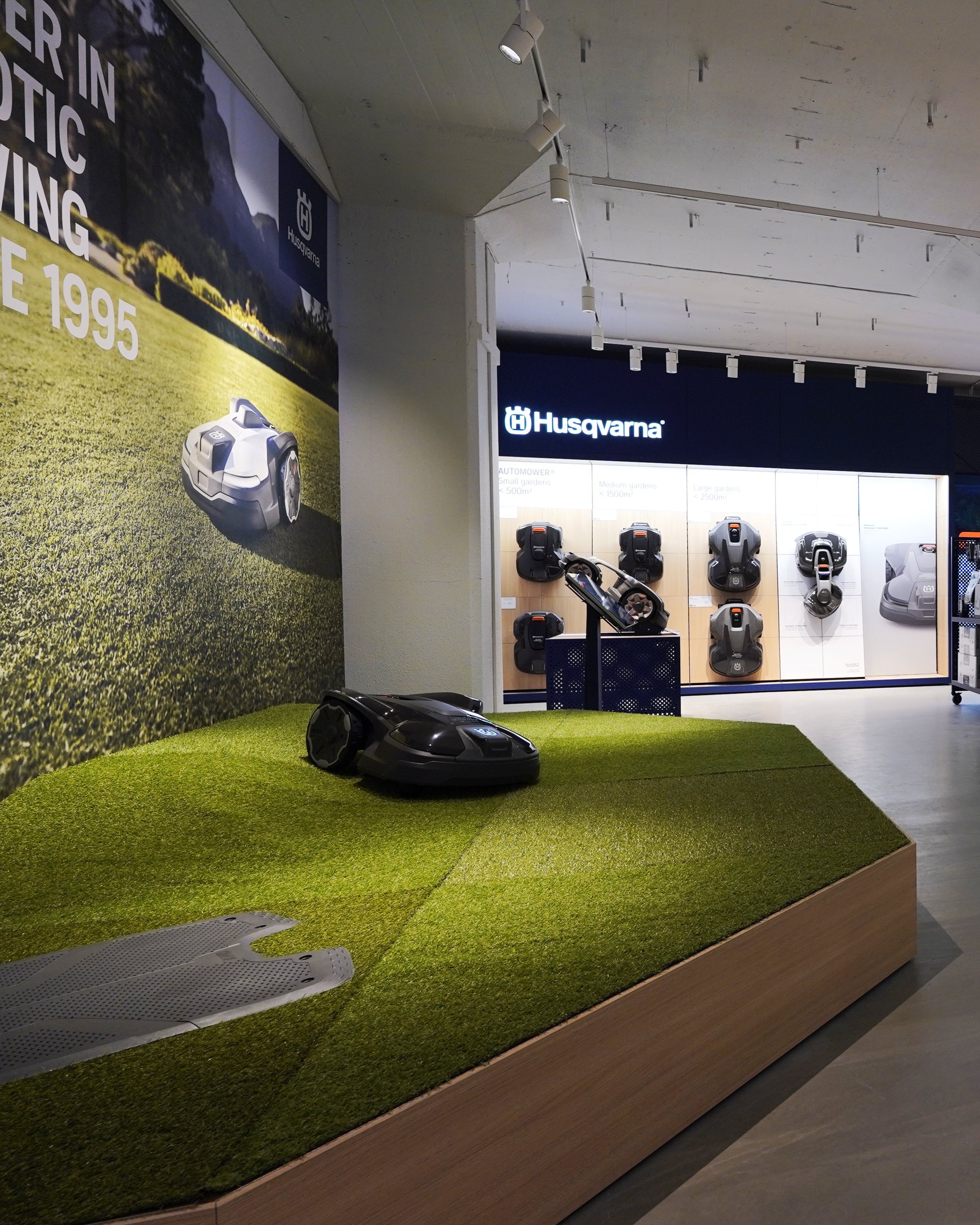 Husqvarna robotic mower display on a raised turf platform in the pilot store