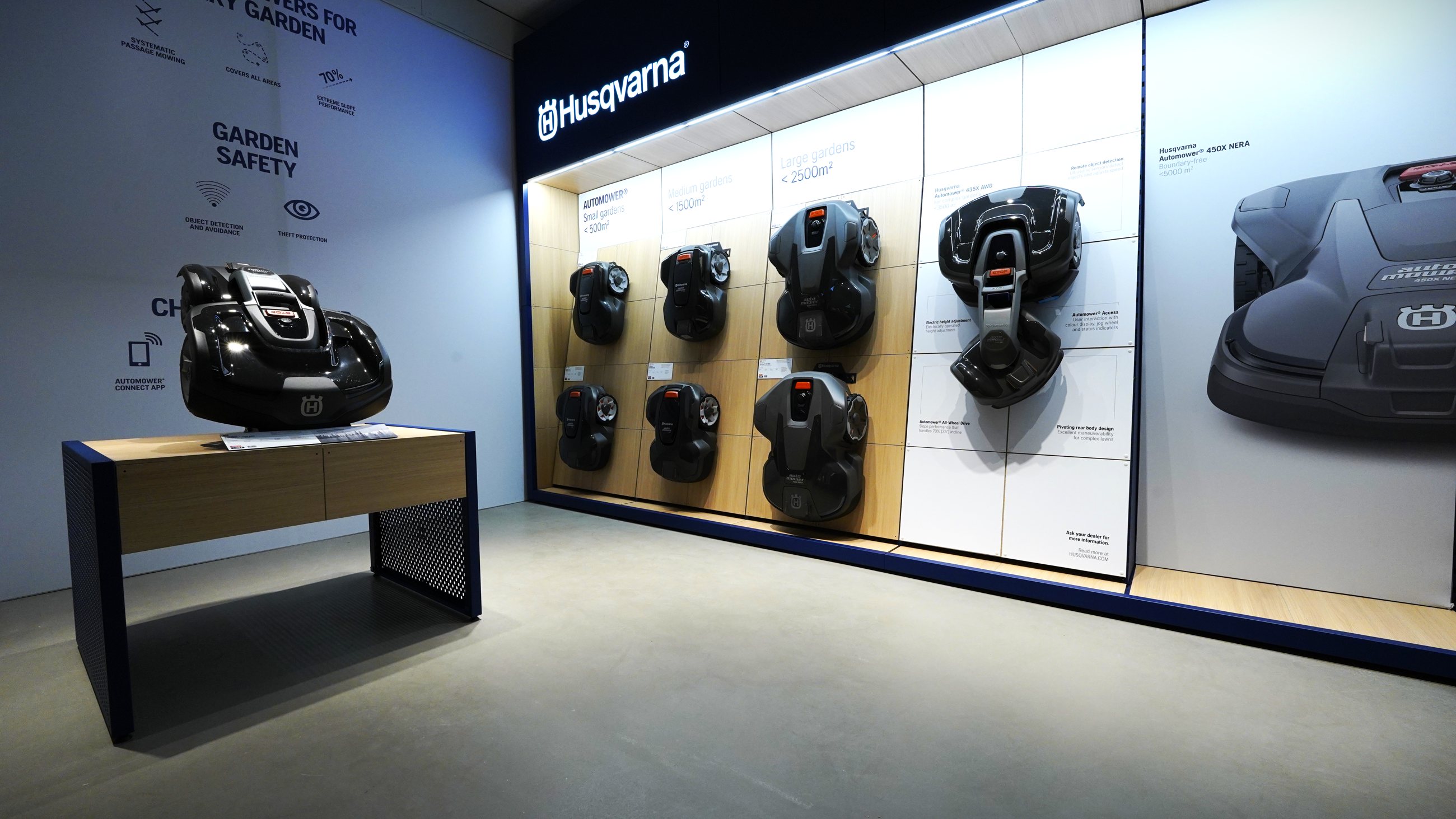 Husqvarna robotic mower range displayed on a light wood and blue wall system