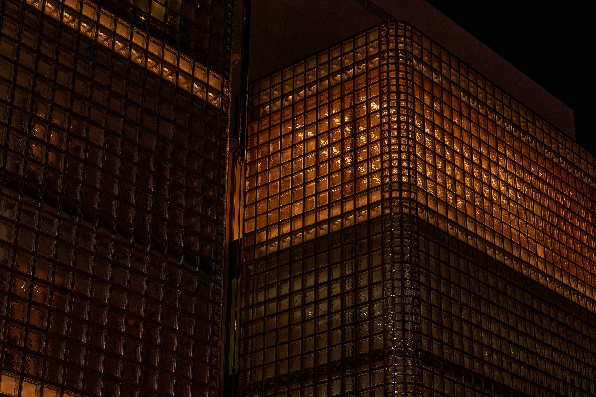 Eine Fassade aus Glasbausteinen, nachts von innen warm durchleuchtet, aus der Untersicht. Foto: Hiroya Nakashima