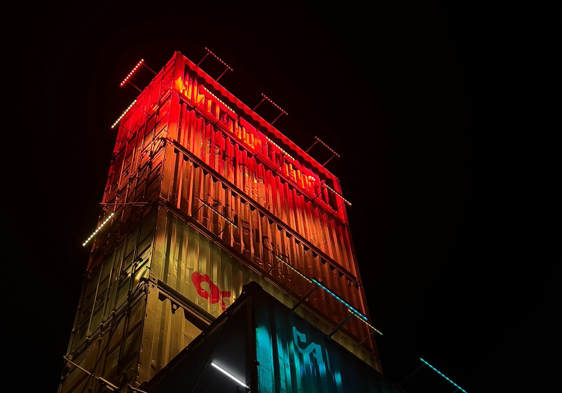 Der Freitag-Turm in Zürich-West, ein Stapel gebrauchter Schiffscontainer, nachts rot und türkis beleuchtet. Foto: Martial Künzler