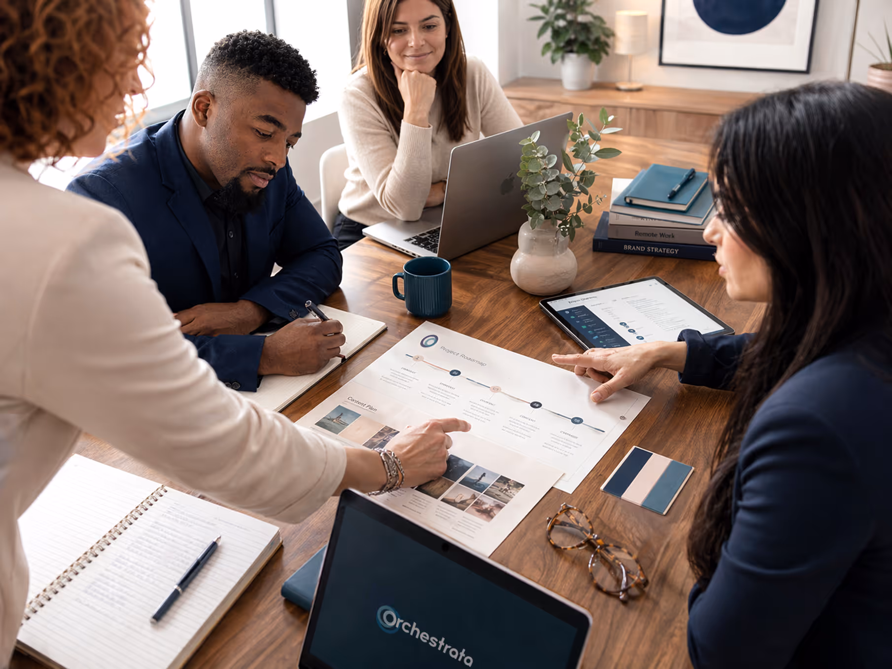 Four diverse professionals collaborating at a wooden table with laptops, documents, and a project roadmap.
