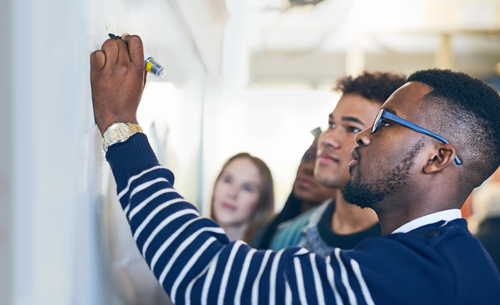 A training participant writes on a whiteboard in front of a group