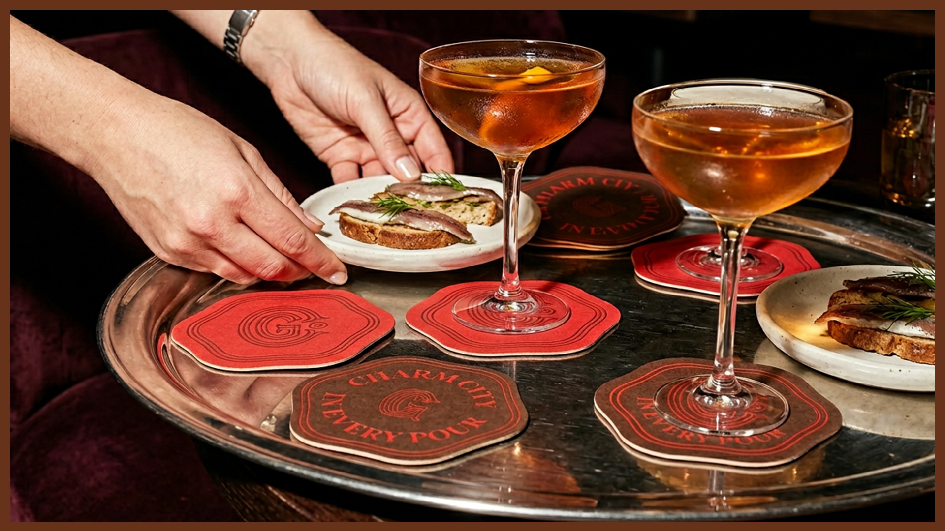 Silver tray holding two cocktail glasses on red and brown coasters and plates with bread topped with anchovies and dill.