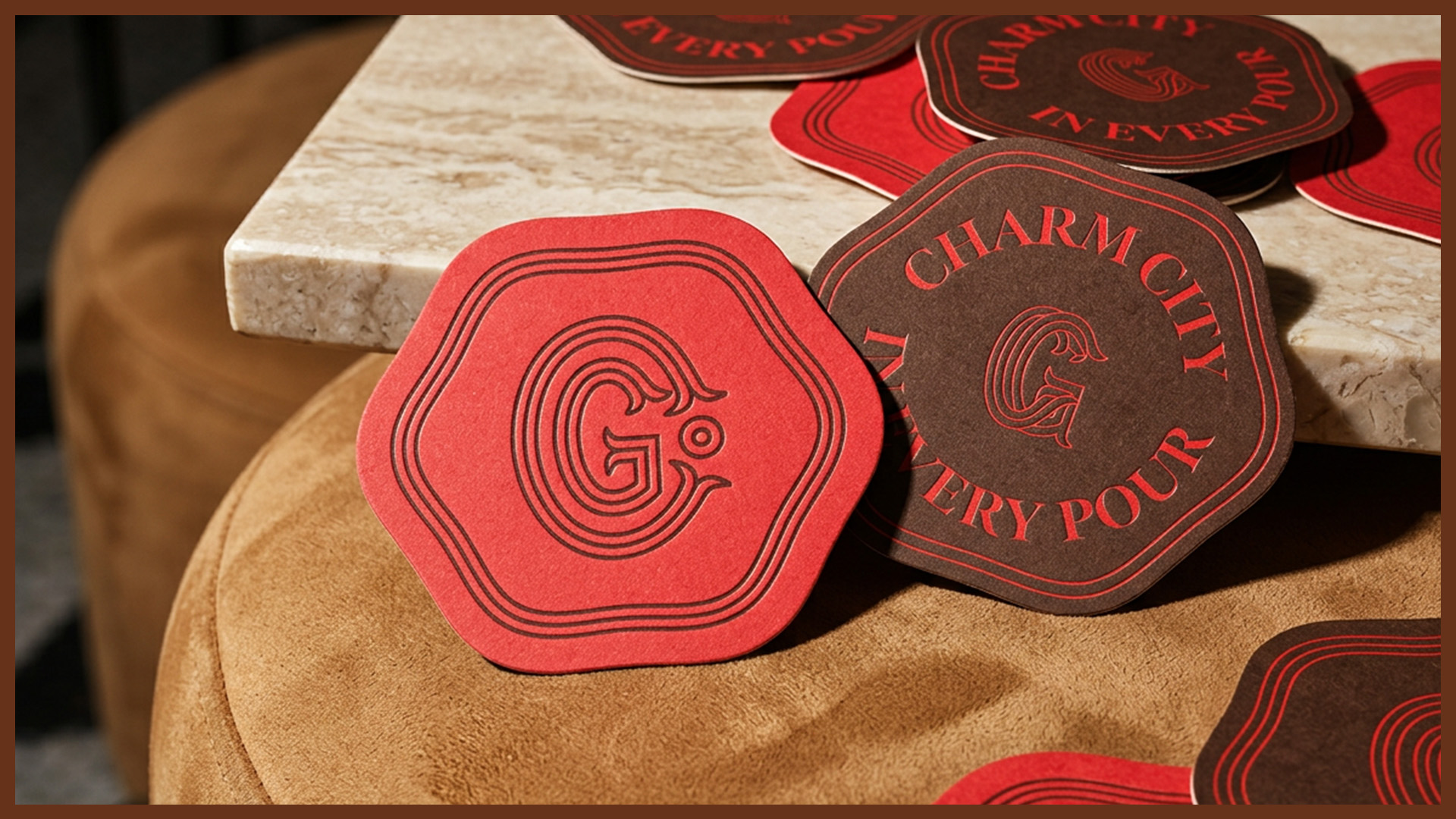 Red and dark brown coasters with the letter G and text 'Charm City In Every Pour' placed on a beige and brown surface.