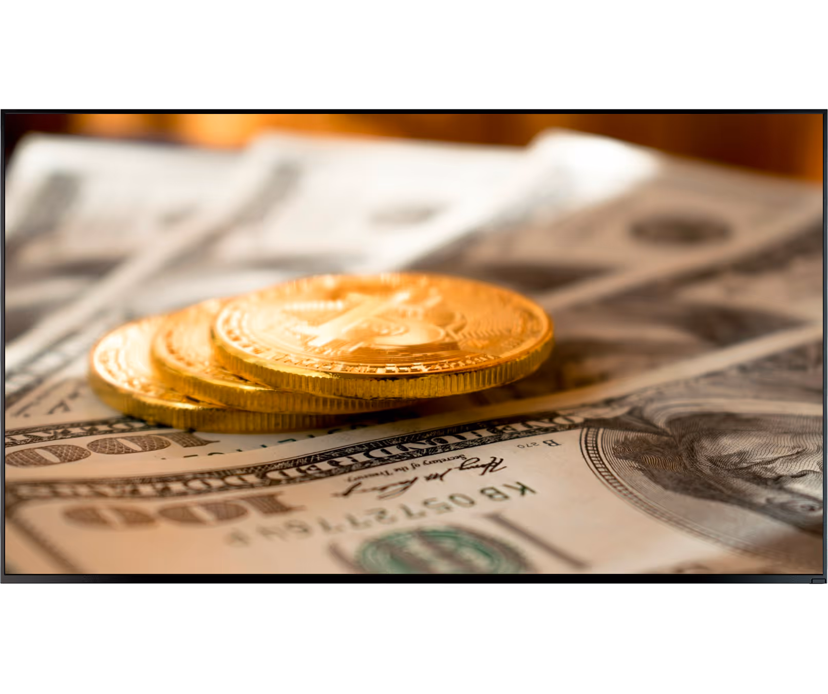 Three gold bitcoins stacked on US hundred-dollar bills with Benjamin Franklin's portrait.
