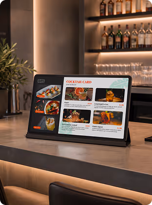 Tablet on bar counter displaying a cocktail menu with images of drinks and prices.