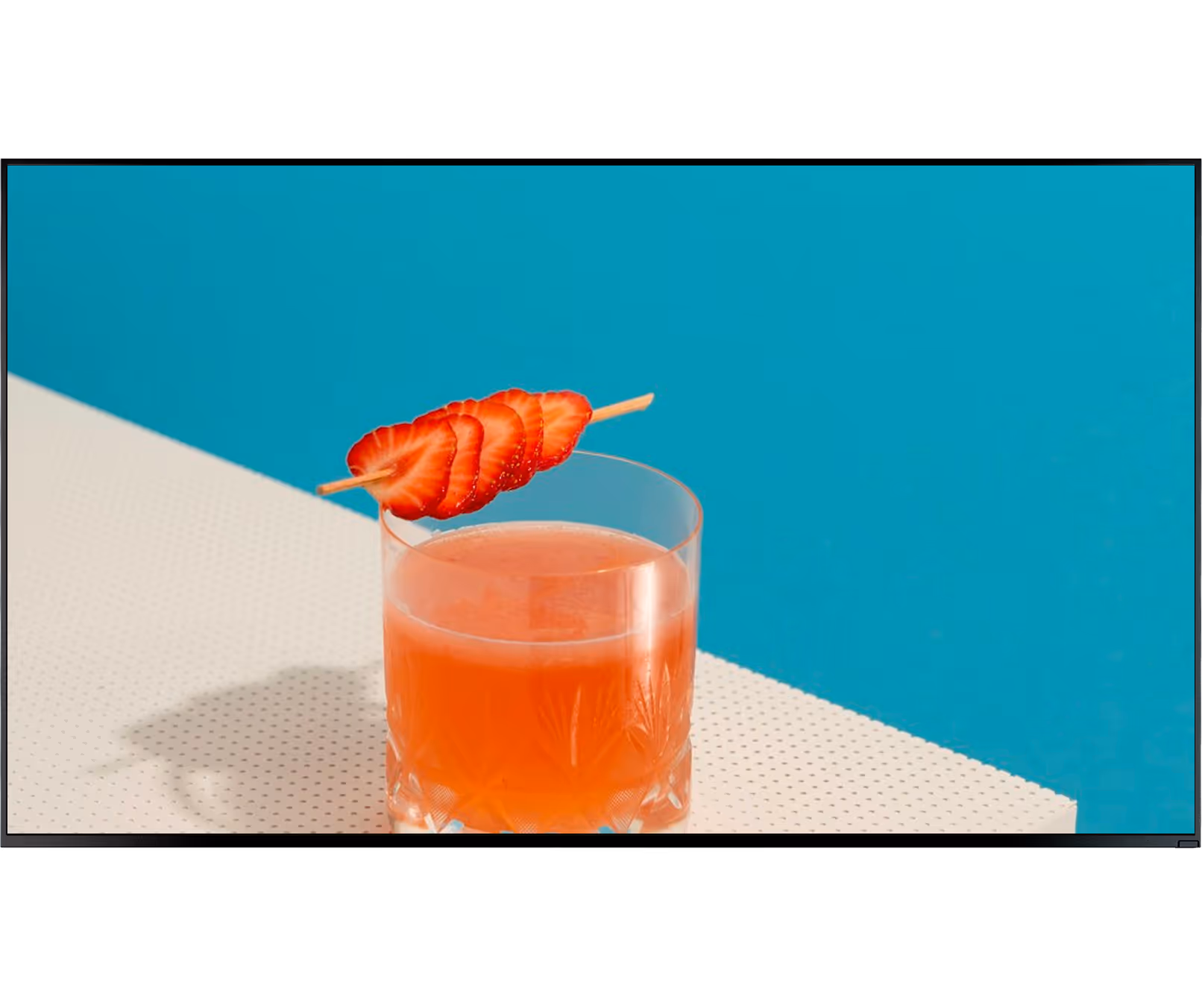 Orange drink in a glass garnished with sliced strawberries on a skewer on white and blue background.