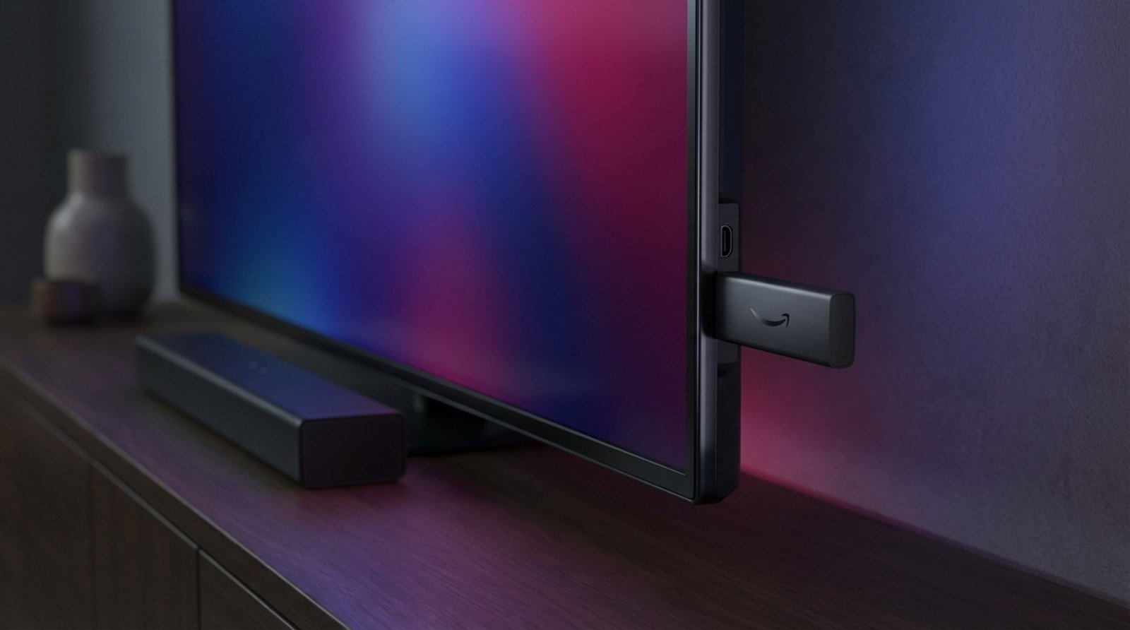 A compact black Fire TV Stick 4K Max plugged into a modern television's HDMI port, with the screen glowing in blue and purple tones.