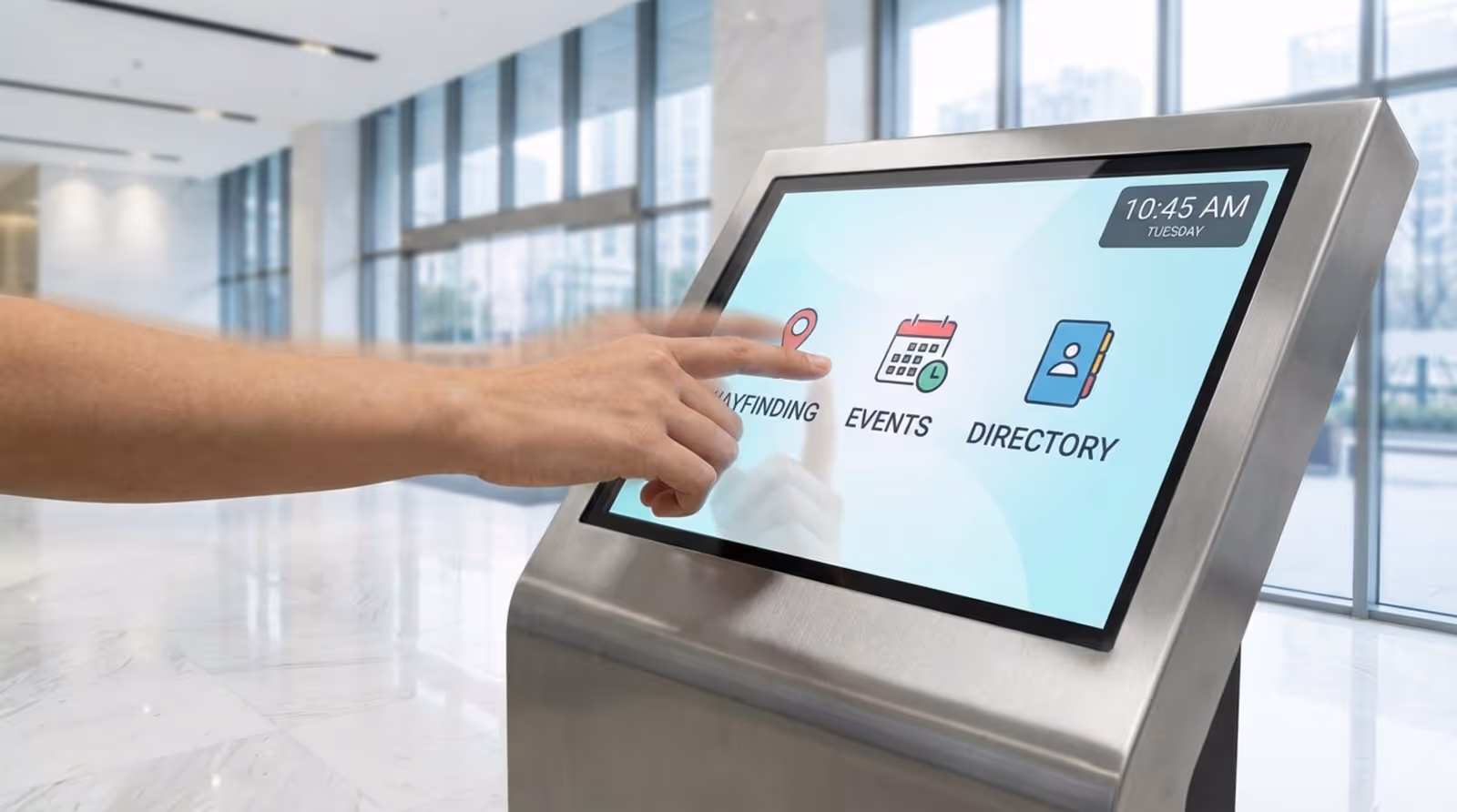 A person's hand interacts with a modern digital signage kiosk in a bright, contemporary lobby showing an intuitive interface.
