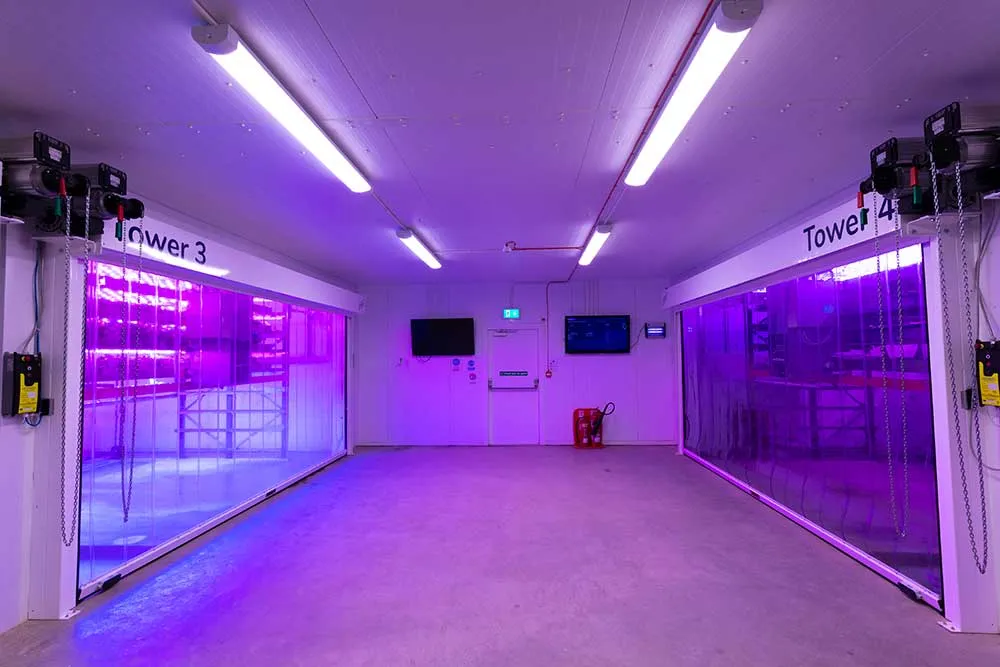 perator uses laptop to manage vertical farm Growth Tower with purple LED grow lights.