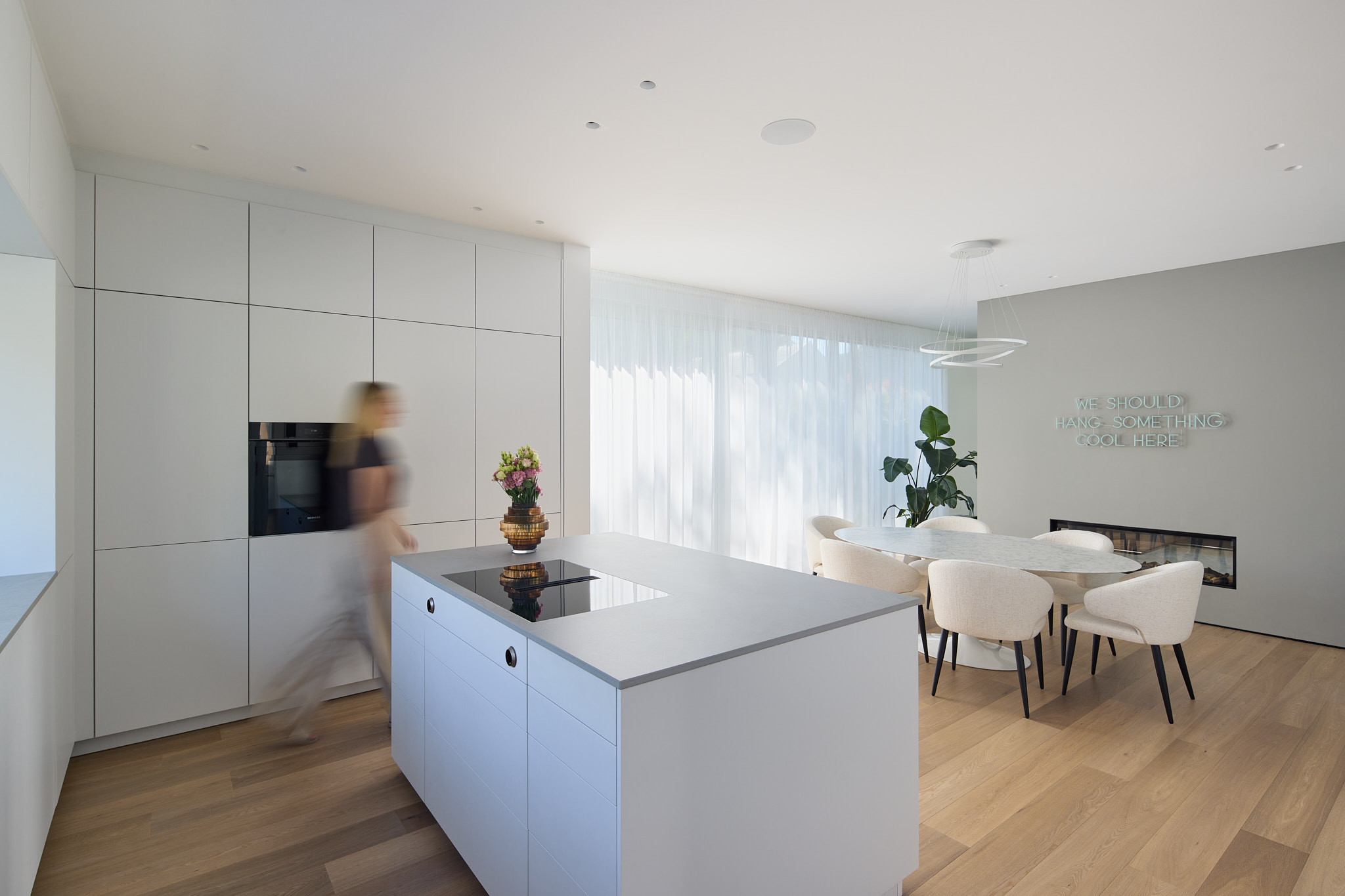 Offener Küchen- und Essbereich, die Bauherrin läuft durchs Bild – moderne Wohnarchitektur.