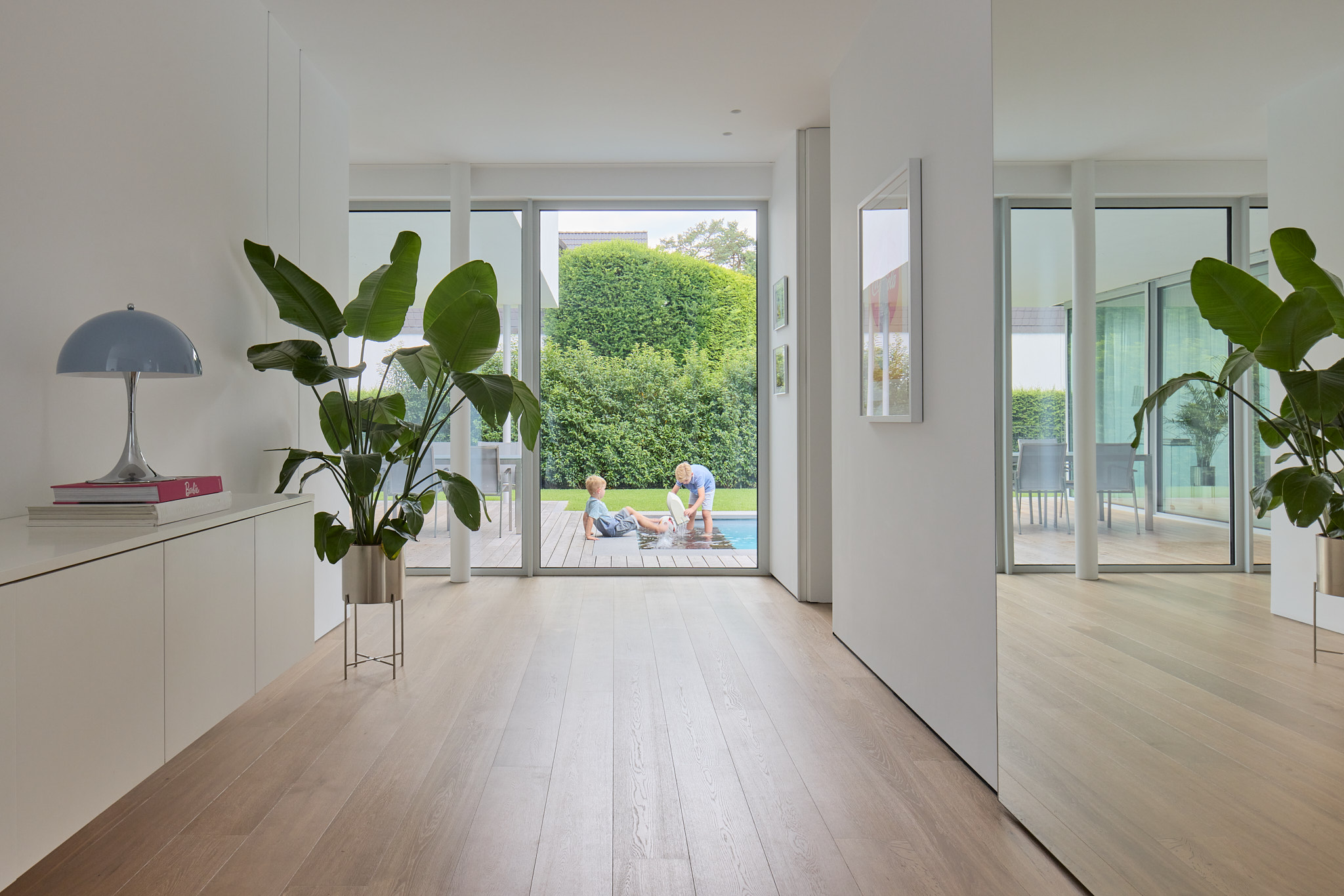Durchblick vom Innenraum auf Terrasse und Pool mit spielenden Kindern.