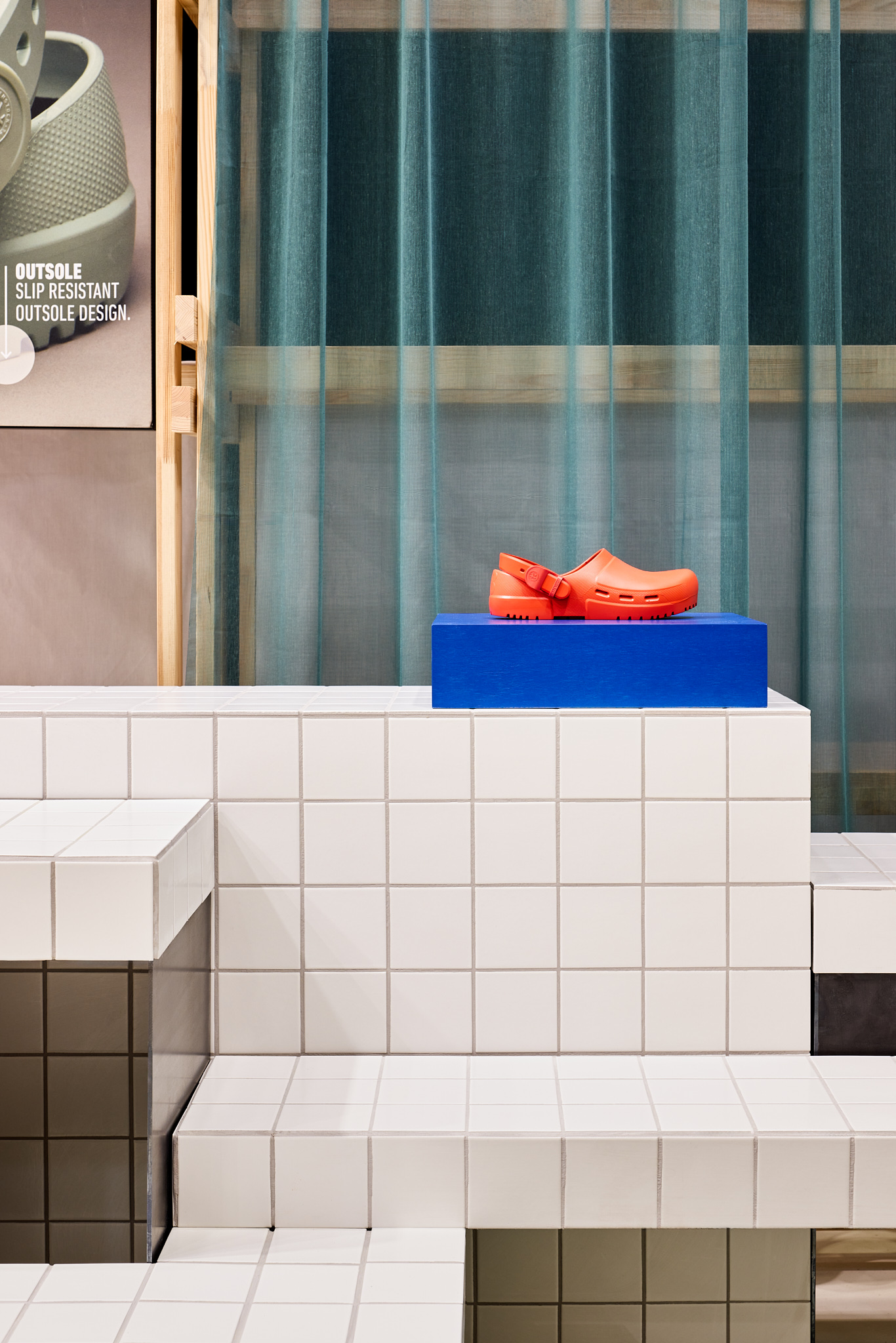 Choral-roter Schuh auf blauem Podest mit weißem Fliesenuntergrund