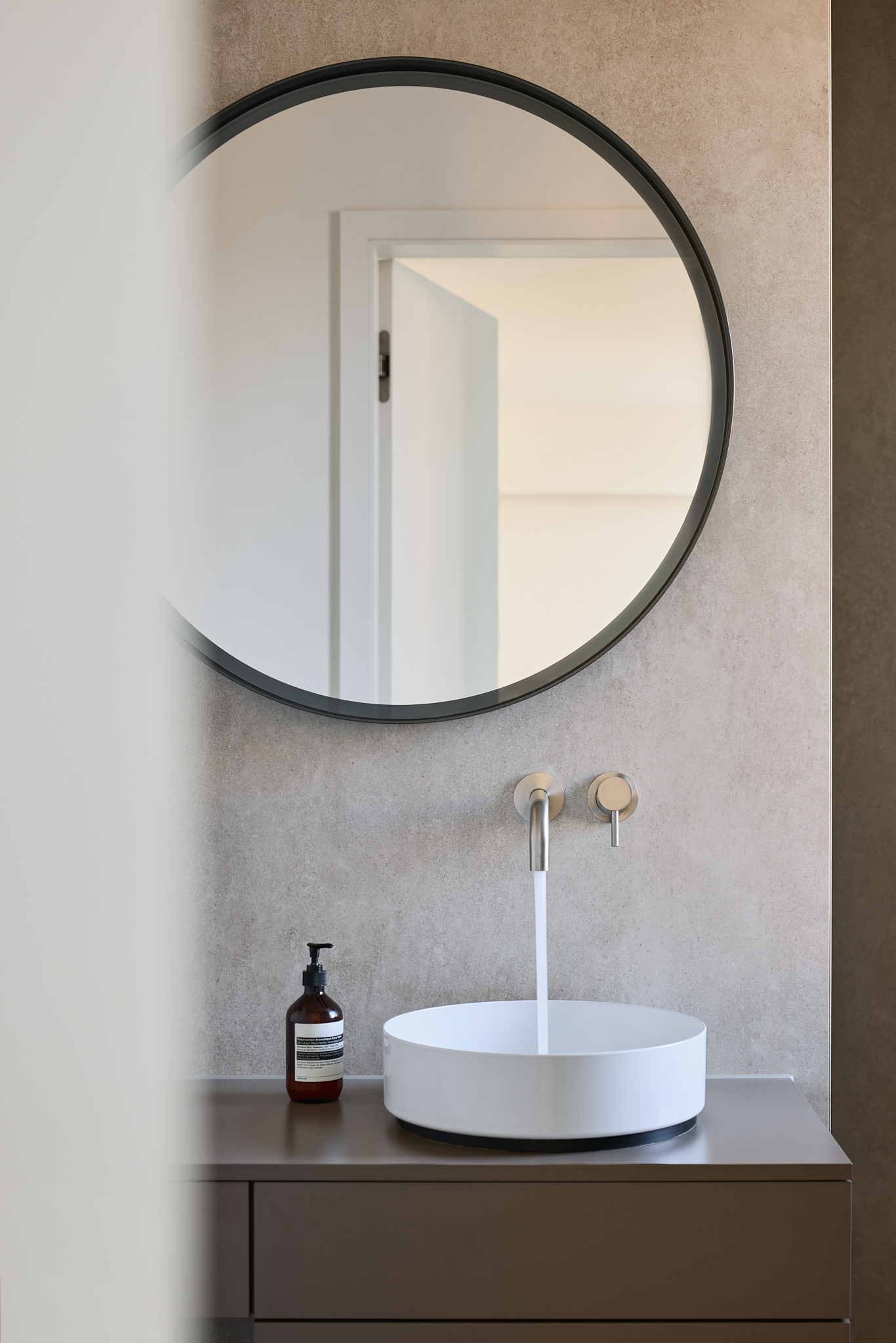 Badezimmer mit rundem Spiegel und laufendem Wasserhahn, atmosphärische Architekturfotografie.