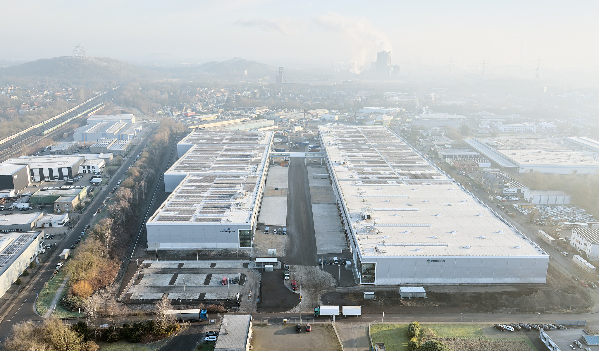 Drohnenaufnahme im Morgenlicht, Blick durch Gebäudeschneise des Logistikzentrums mit verbindender Brücke.