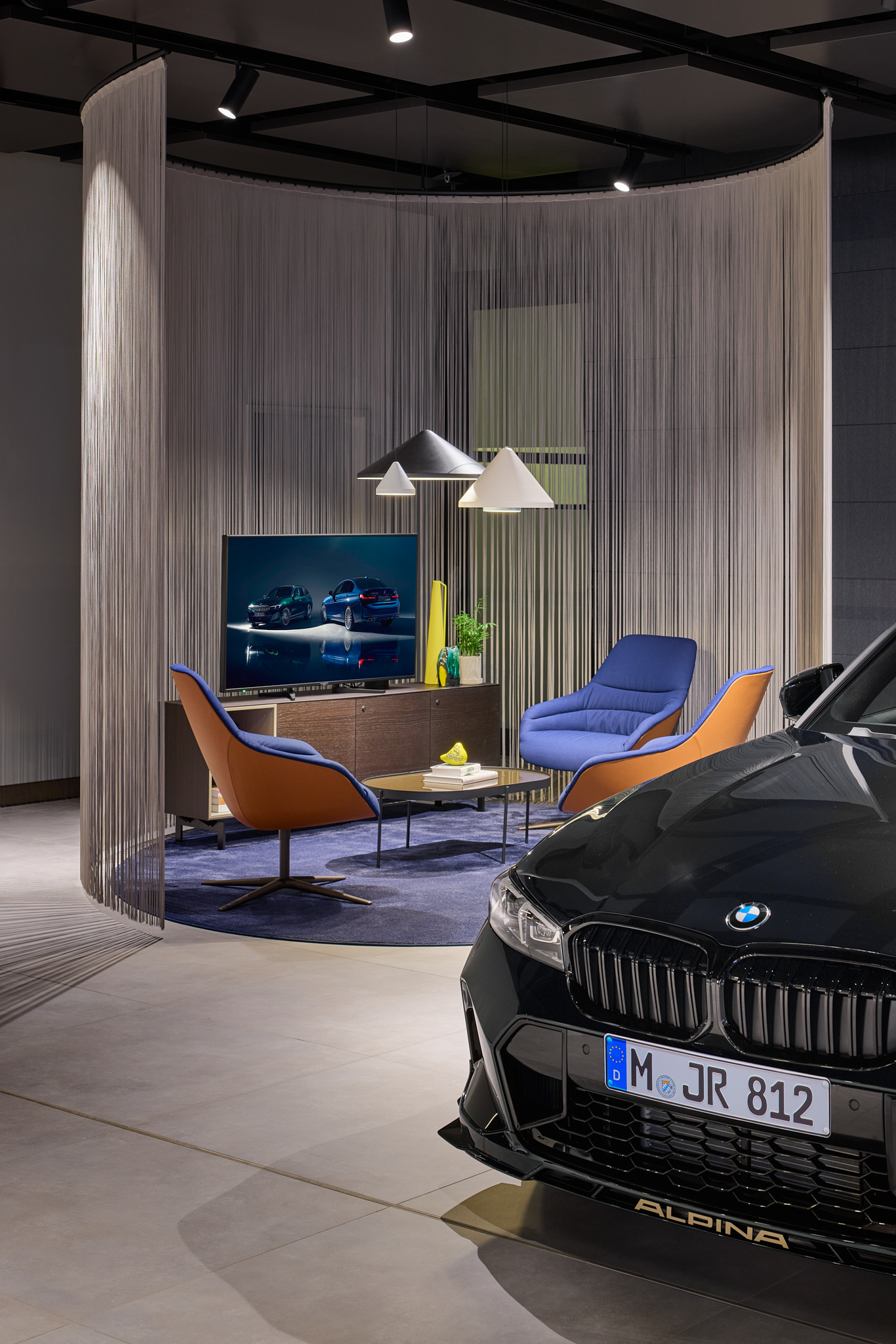 Lounge mit Schalensesseln und Fadenvorhang, BMW im Hintergrund, klare Architekturfotografie.