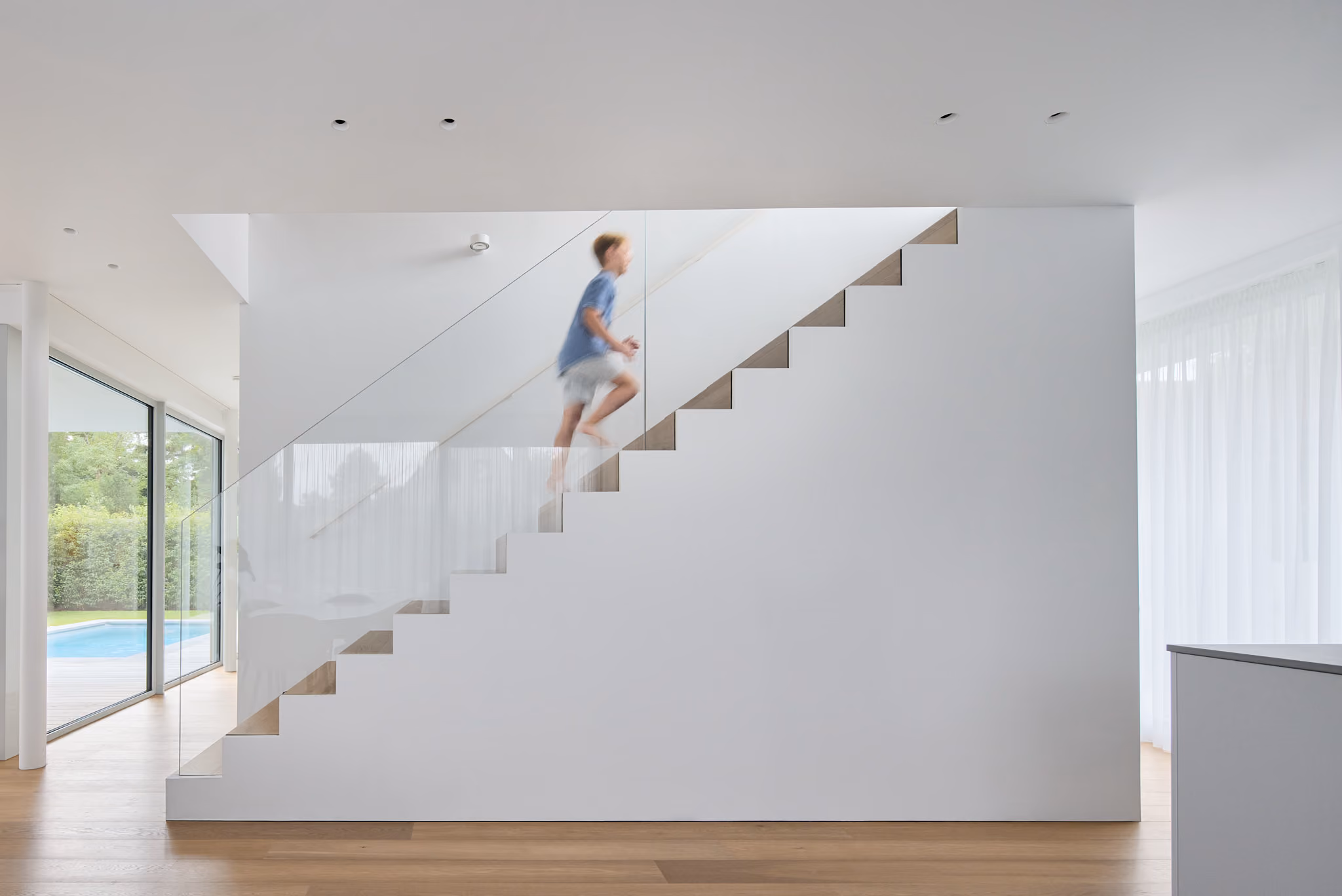 Ein Junge läuft eine moderne weiße Treppe mit Glasgeländer in einem hellen Haus hinauf.