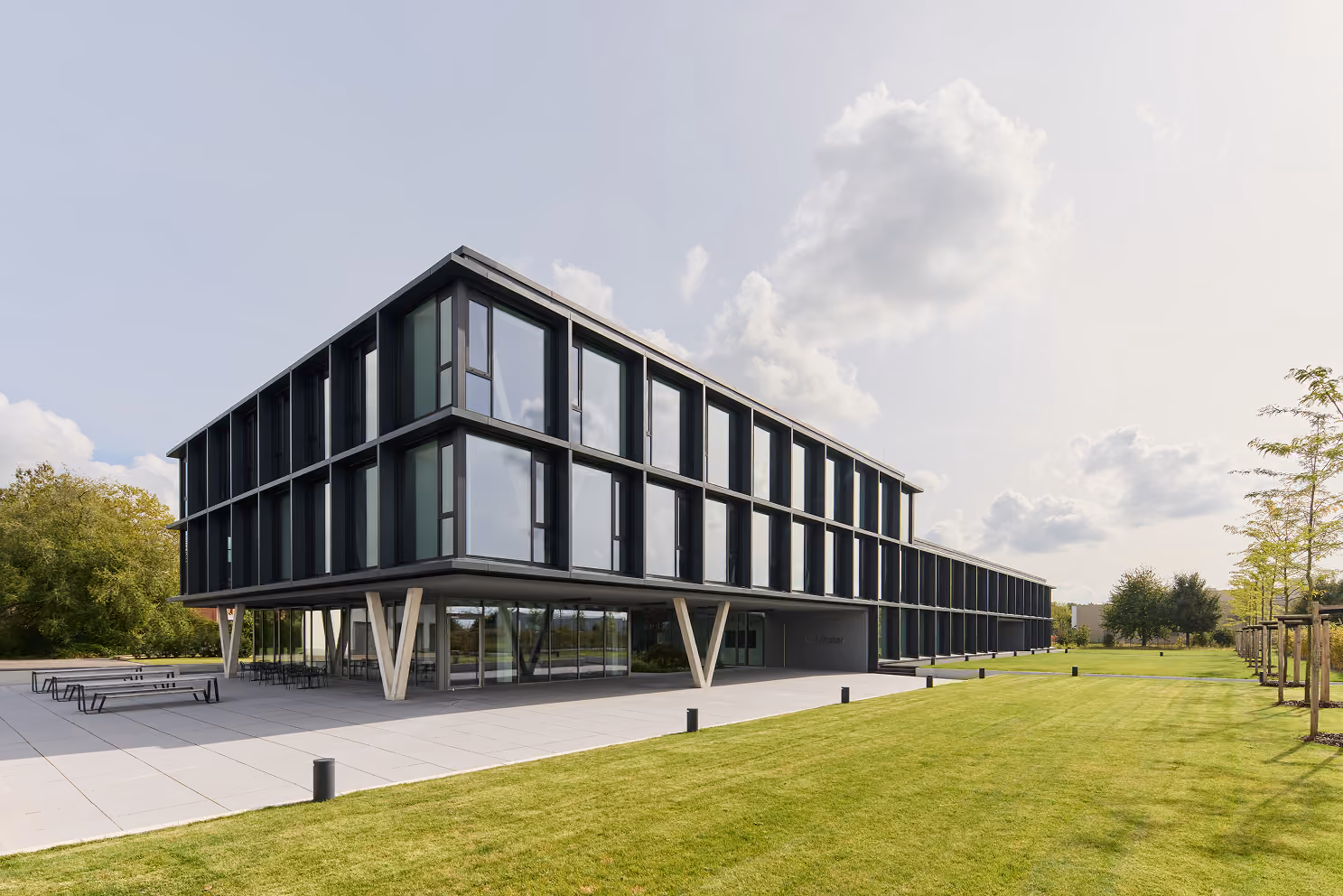 Modern Bürogebäude mit großen Glasfenstern, Betonstützen und gepflegt grünem Rasen.