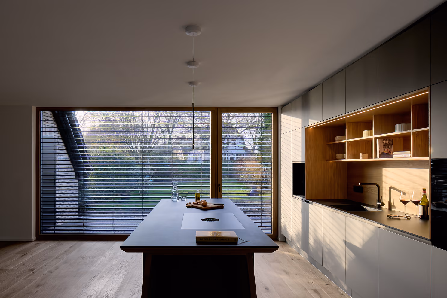 Moderne Küche mit großem Fenster, Kücheninsel, Holzregalen, Spüle, Weinflasche und zwei Gläsern.