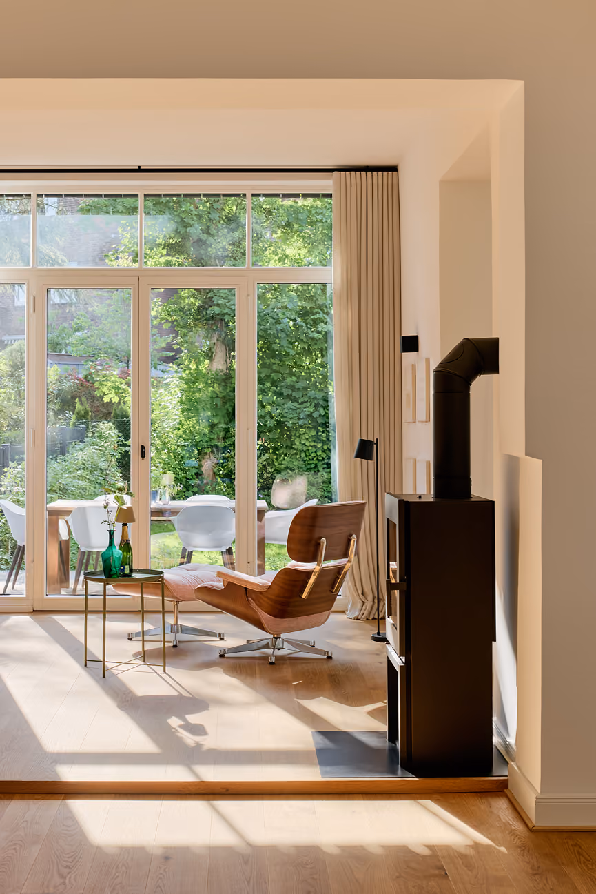 Moderner Wohnraum mit Ledersessel, Ofen, großen Fenstern und Blick auf grünen Garten.