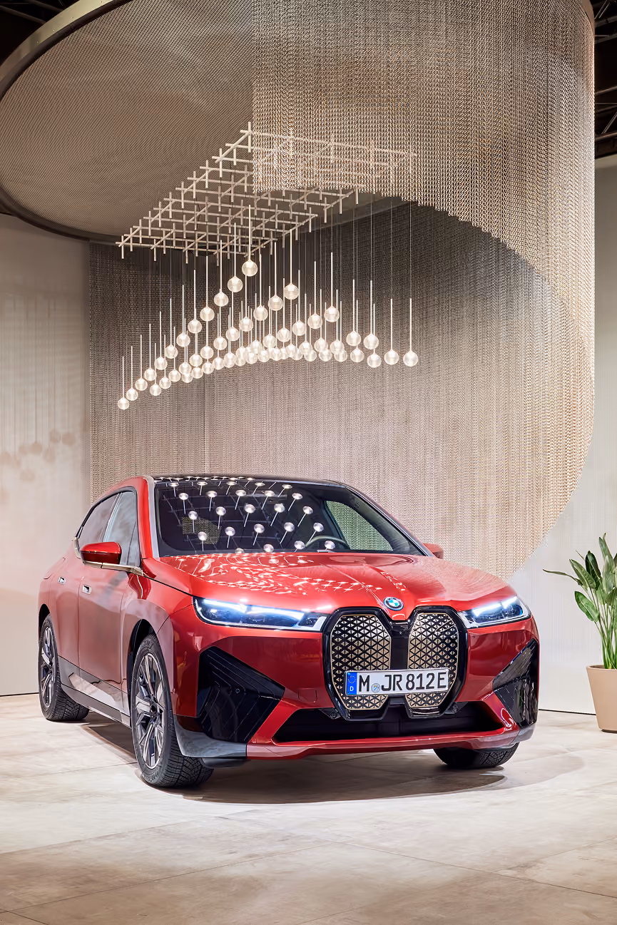 Rotes BMW-Elektrofahrzeug vor moderner Installation mit hängenden Lichtern in Innenraum.