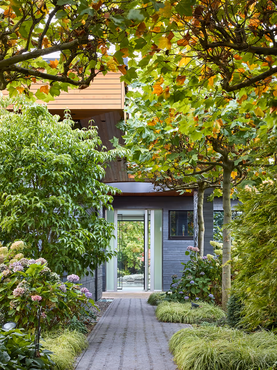 Weg durch grünen Garten mit Bäumen und Blumen zu modernem Haus mit Glas-Eingang.