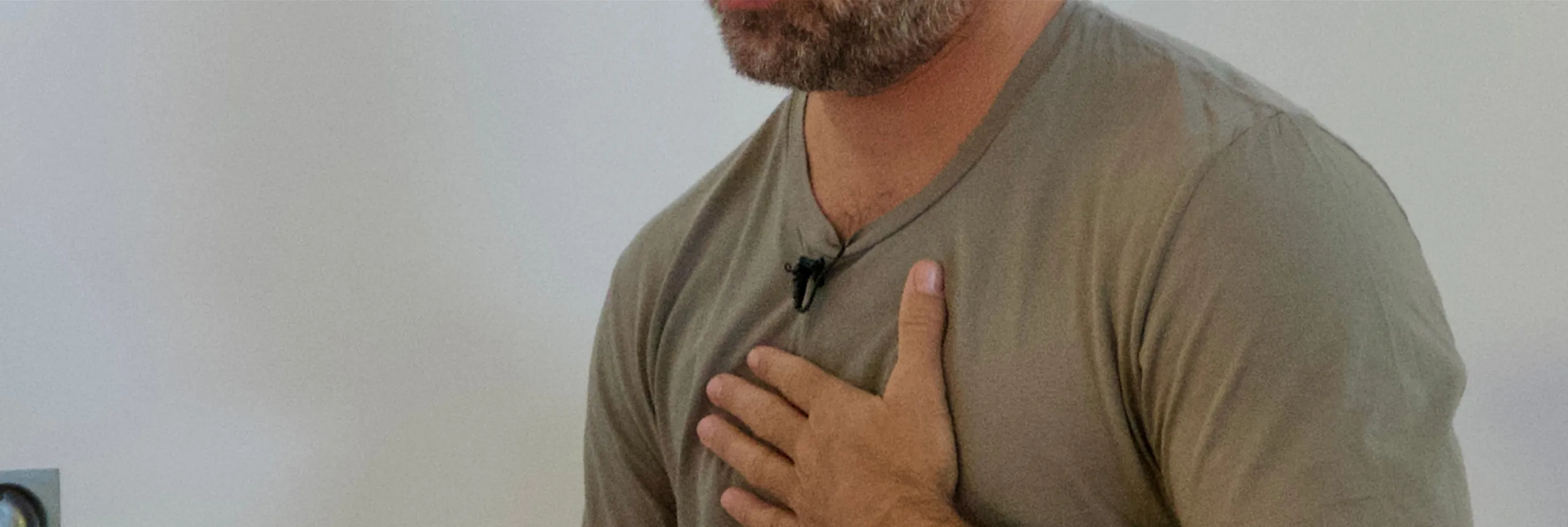 Nat Sharratt holding his chest, wearing a green shirt and a clip-on microphone.